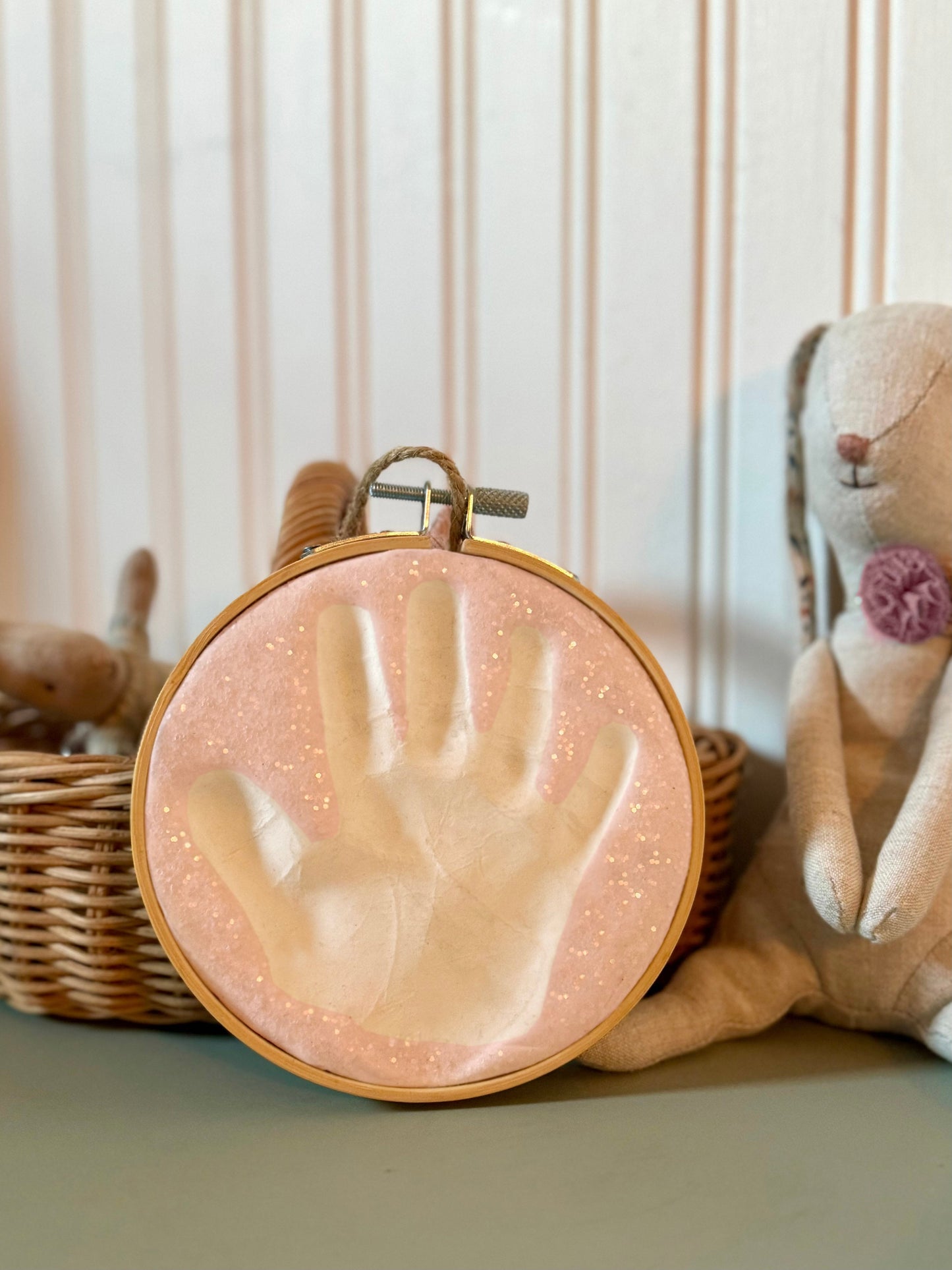 Handprint keepsake with glitter detail displayed on a shelf beside a stuffed bunny