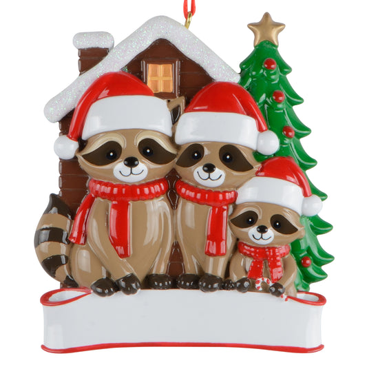 Raccoon Family of 3 Christmas ornament showing three raccoons wearing red Santa hats and scarves in front of a snowy cabin and decorated Christmas tree