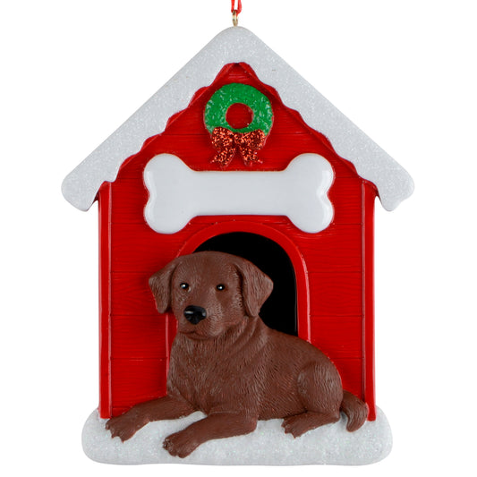 Chocolate Labrador Retriever dog lying in front of a red doghouse ornament with white snow and a green wreath, hanging on a red ribbon