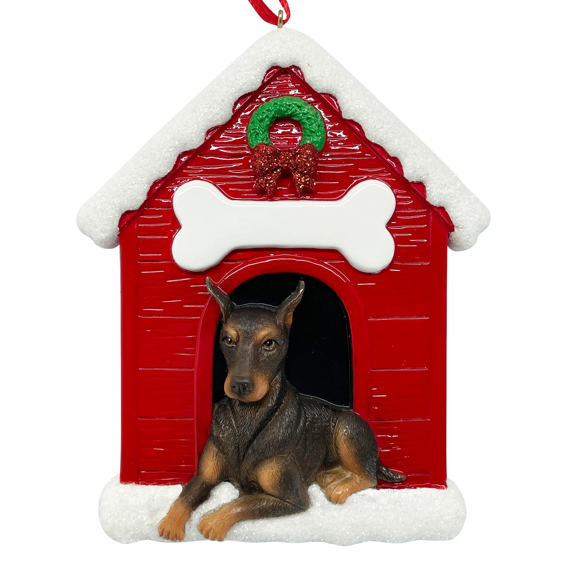 Handpainted Doberman Pinscher ornament lying in front of red doghouse with white snowy roof and festive wreath