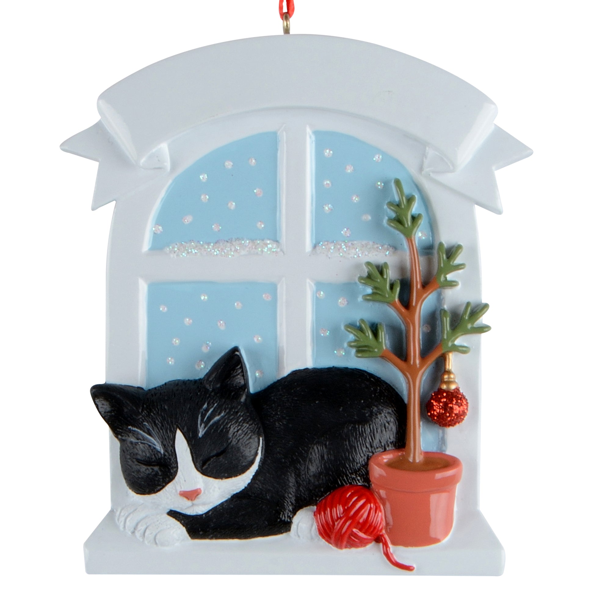 Handpainted holiday ornament featuring a sleeping tuxedo cat by a snowy window with a small potted holiday tree and red yarn ball