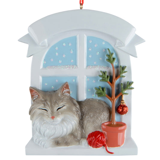 Handpainted holiday ornament featuring gray Maine Coon cat resting by snow-covered window with potted tree and red yarn ball