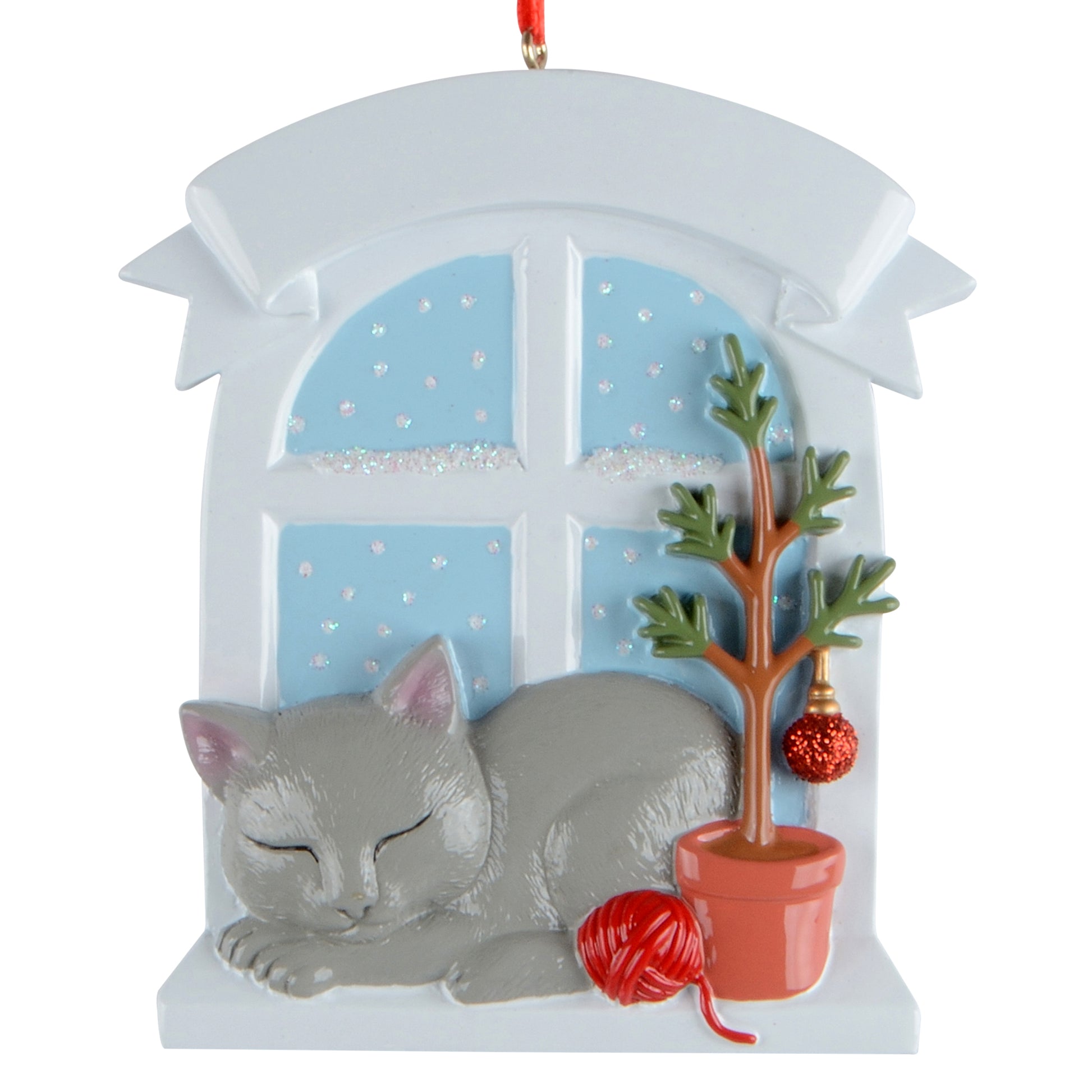 Handpainted gray cat ornament resting on a windowsill with snowy window background, potted tree, and red yarn ball.