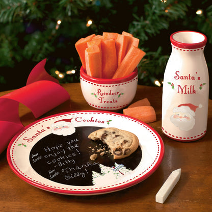 Close-up of the Santa message plate with chalk writing, milk jug labeled 'Santa's Milk,' and reindeer treat bowl filled with carrot sticks set on a wooden table with a Christmas tree in background