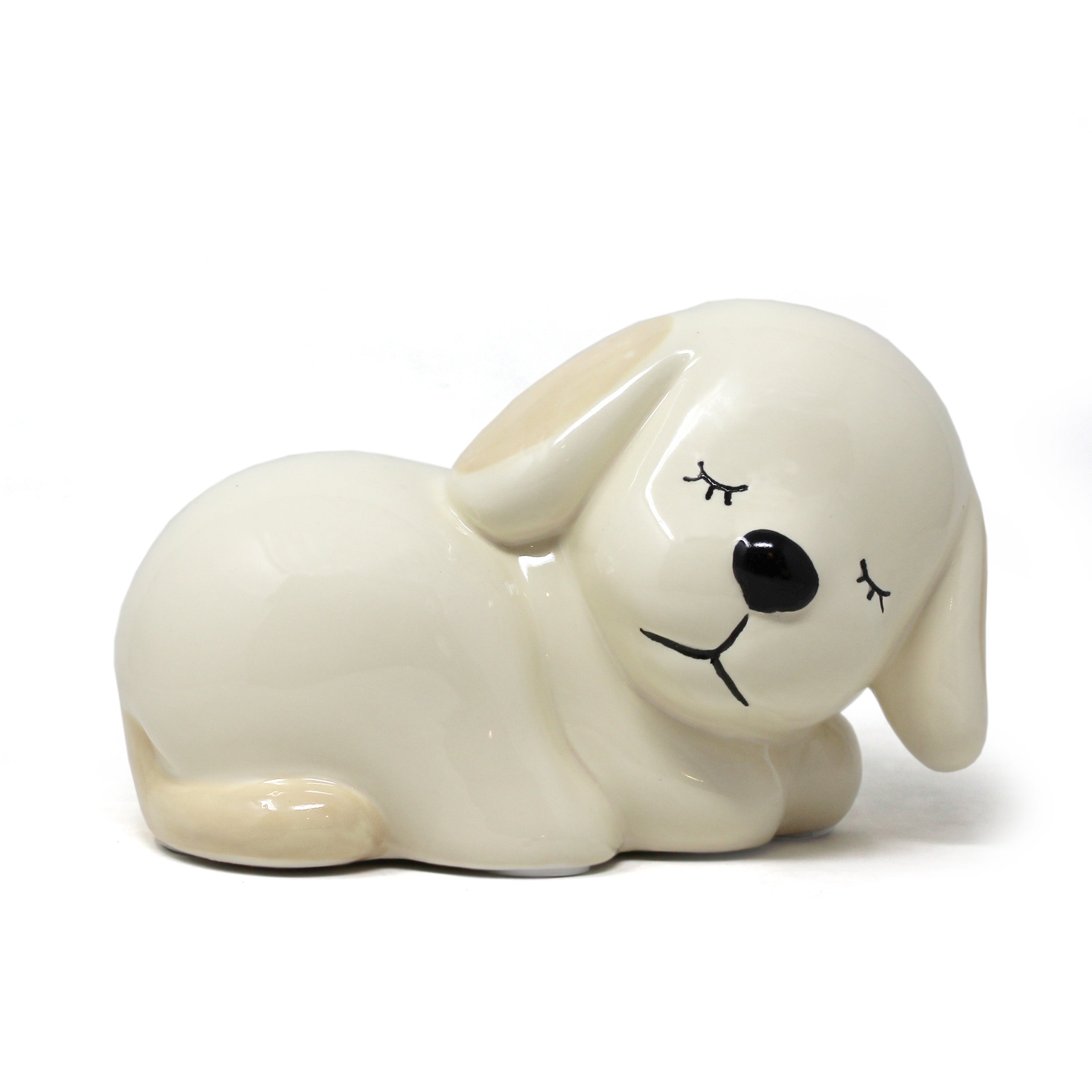 Handpainted ceramic sleeping puppy piggy bank in cream with beige accents and a glossy finish, showing a peaceful closed-eye expression