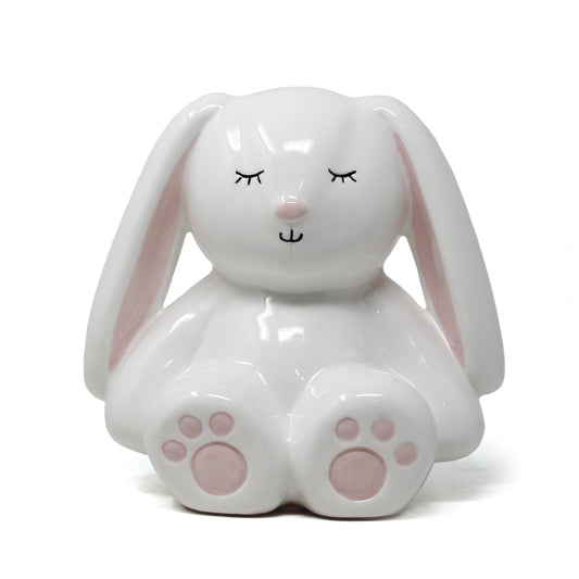 White ceramic bunny piggy bank with pink ears and paw pads and closed eyes