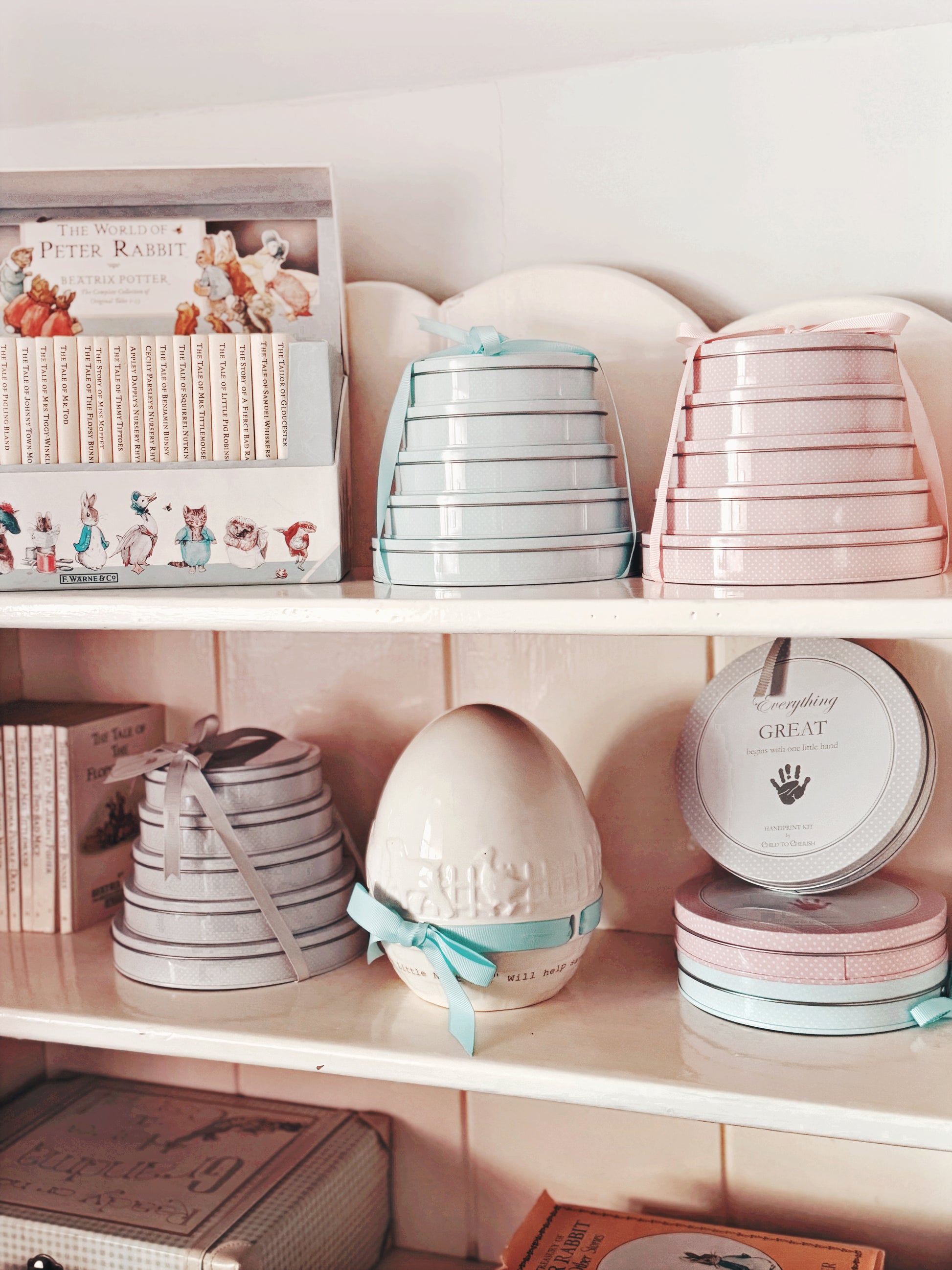 Three sets of handprint tins in pink, blue, and gray displayed on home shelves