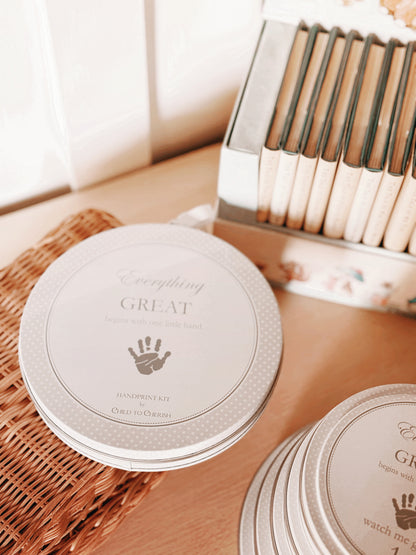 Gray handprint kit on woven surface near vintage books and decorated with polka dots