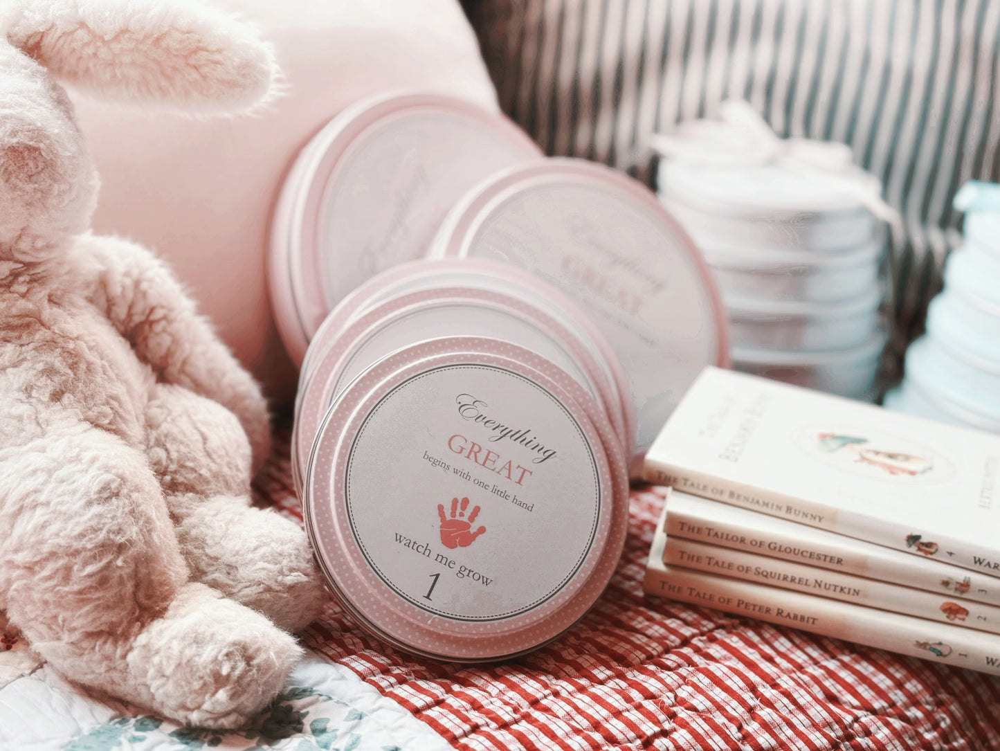 Pink handprint kit tins arranged on a soft blanket with children's books nearby