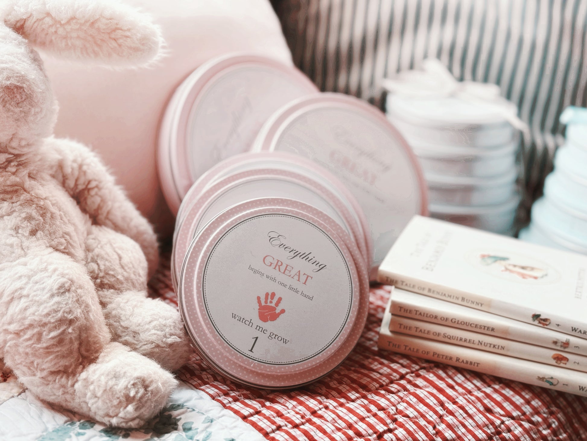 Pink handprint kit tins arranged on a soft blanket with children's books nearby