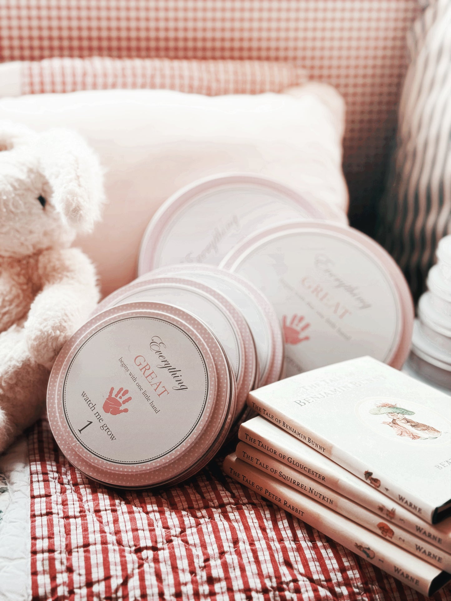 Close-up of stacked pink handprint kit tins on plush surface with books in the background