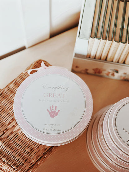 Pink handprint kit placed in wicker basket near books on wood shelf