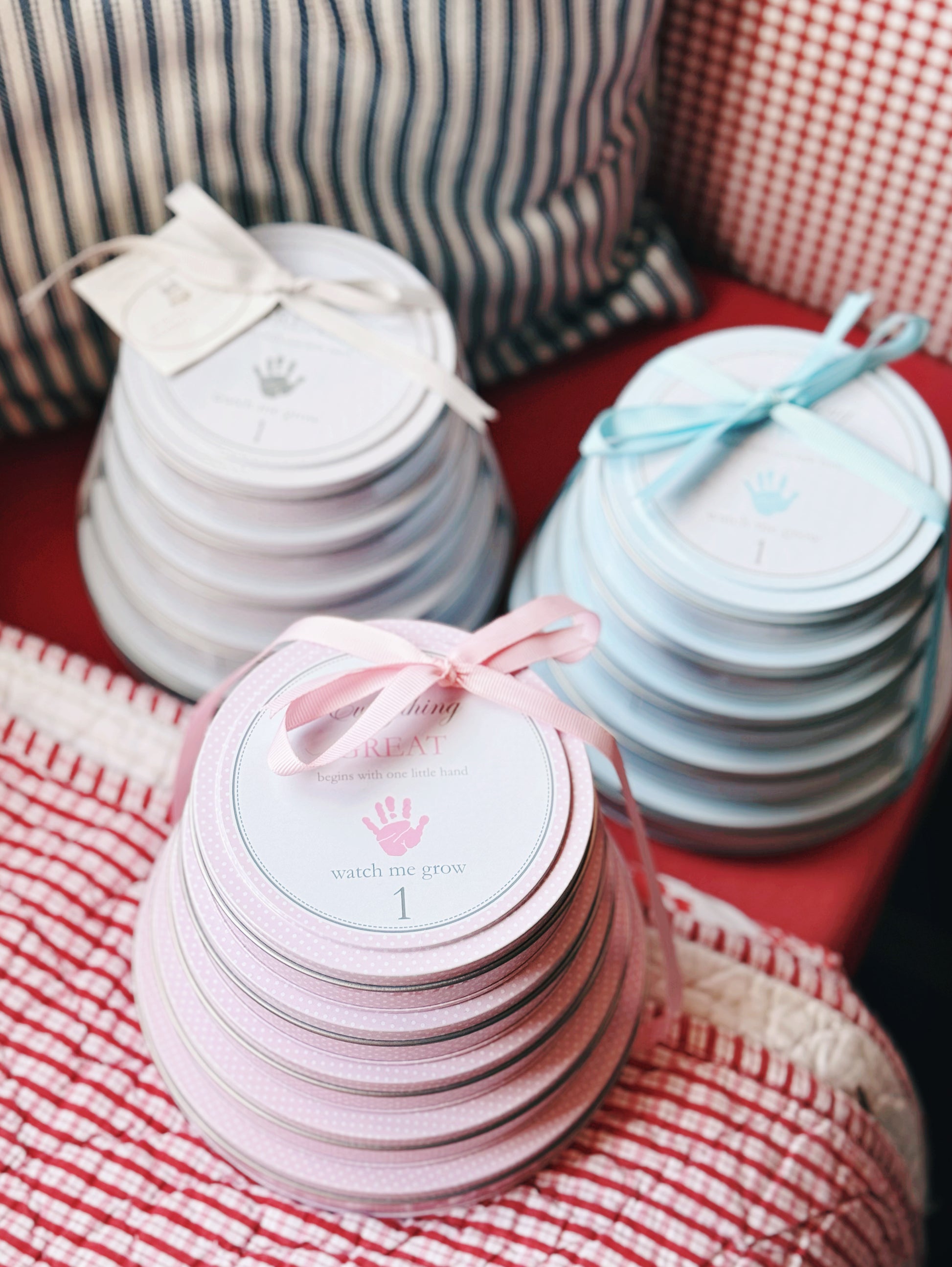 Stacked pink and blue handprint tins next to two gray handprint tins