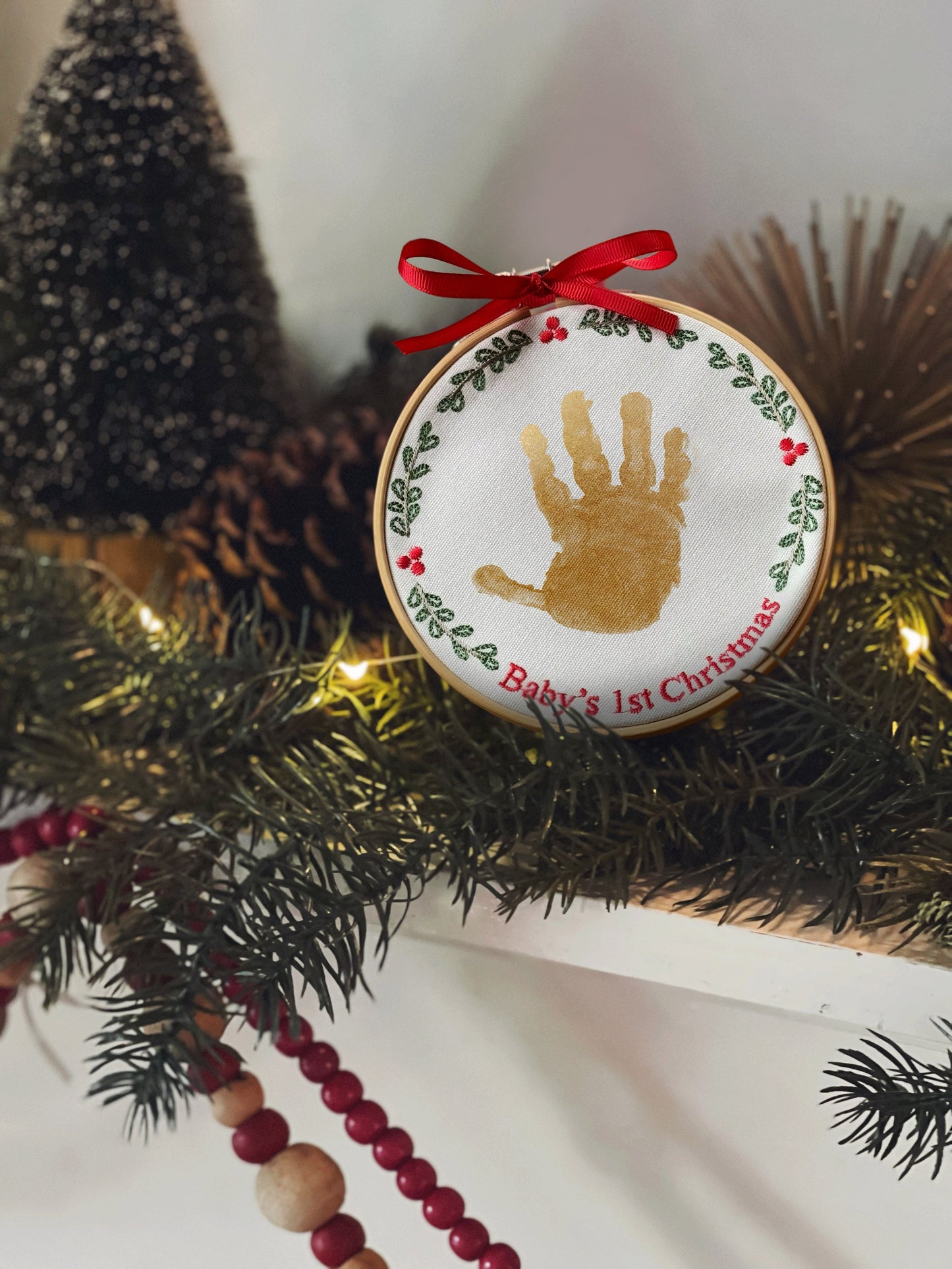 Handpainted baby handprint Christmas ornament displayed on greenery with festive decorations