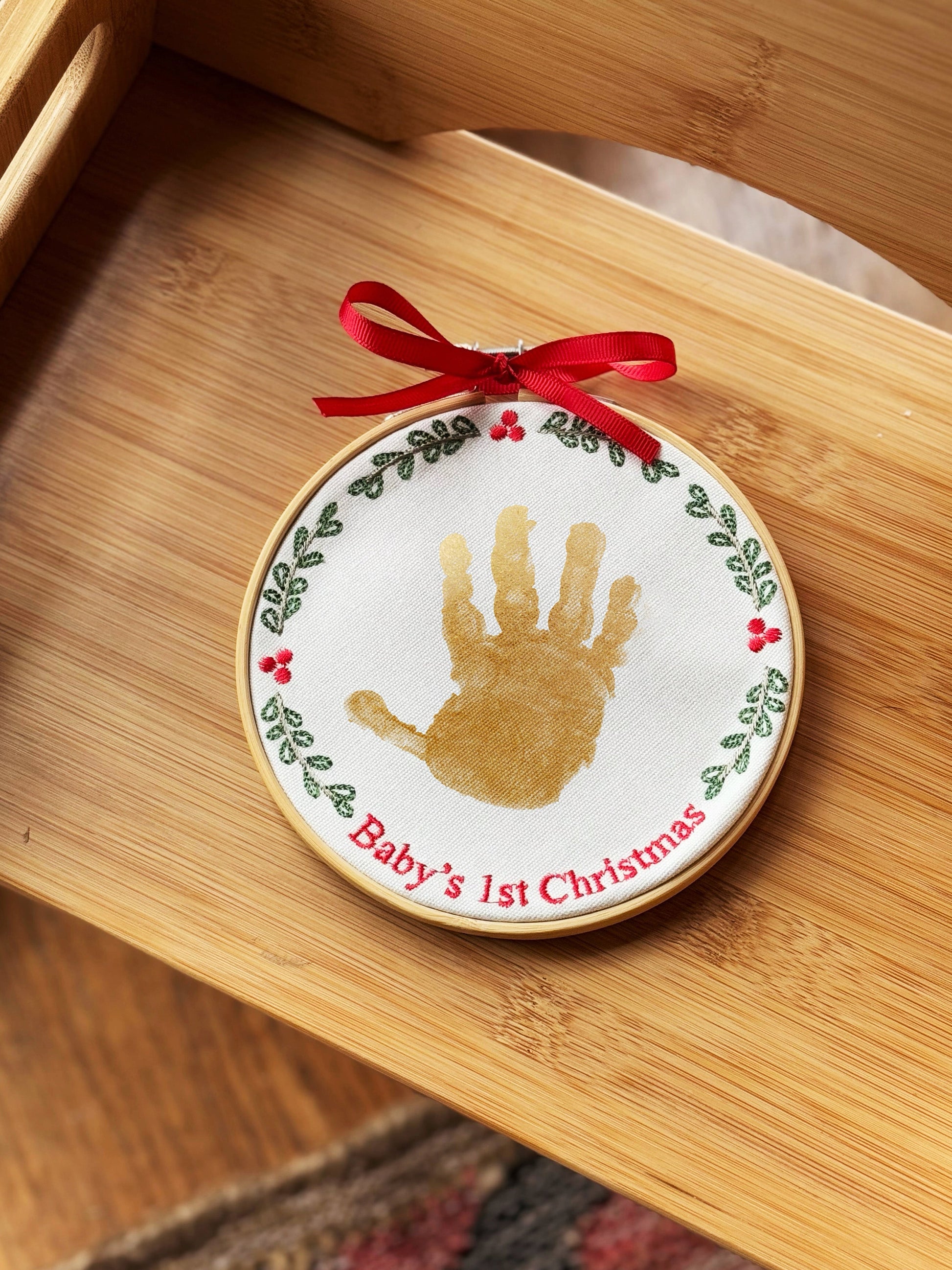 Handprint ornament with gold handprint and embroidered wreath on wooden surface