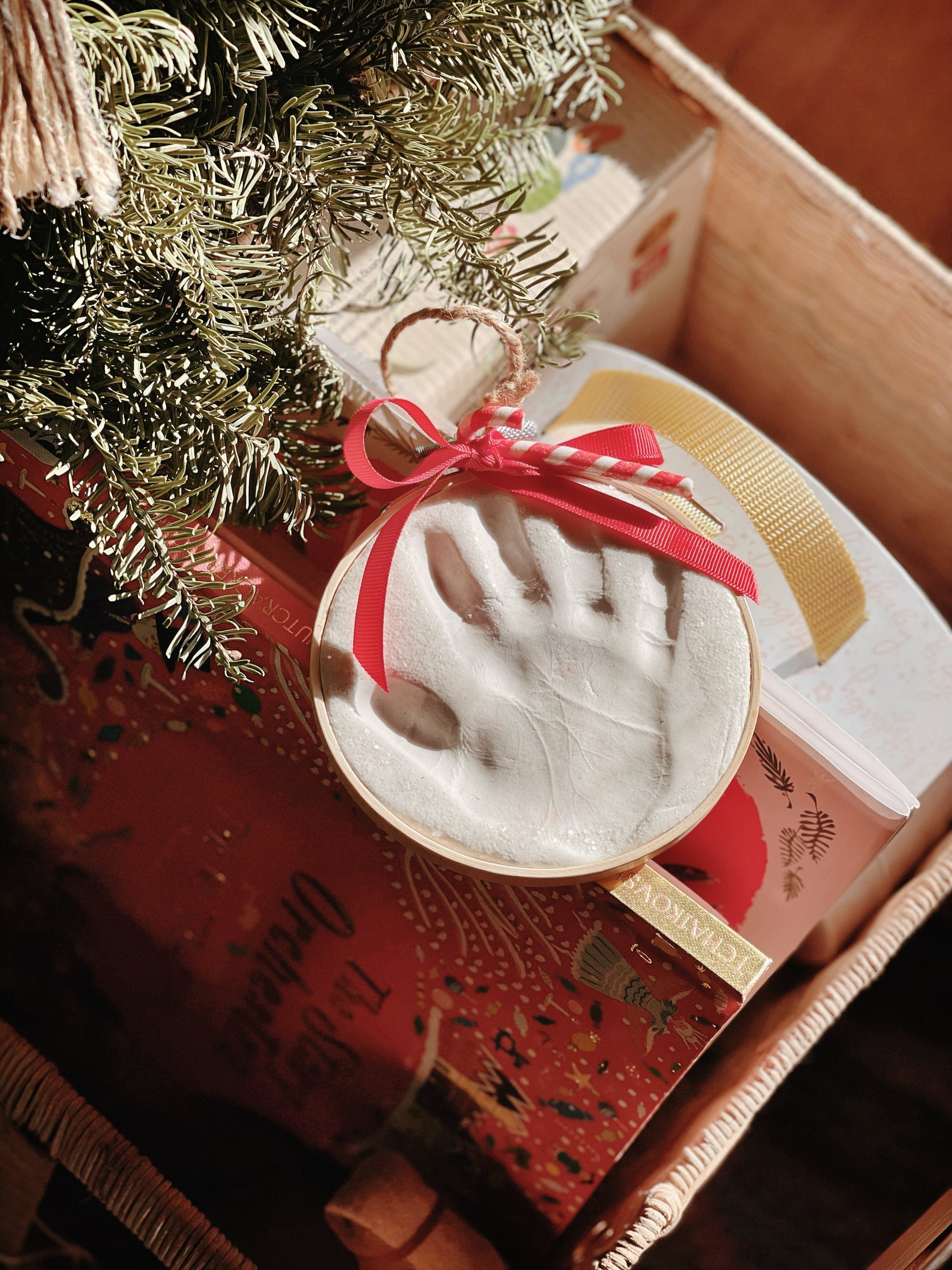 Handprint ornament displayed with Christmas gifts and evergreen branches in a cozy holiday setting