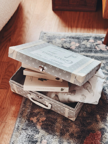 Open gray kids suitcase containing children's books, blanket, and soft toy bunny on wood floor