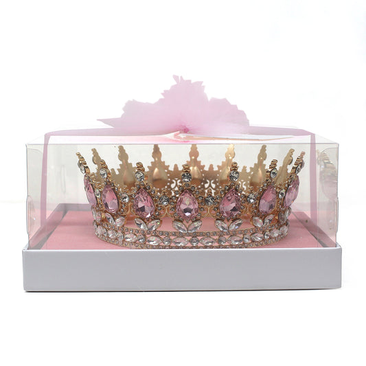 Golden crown adorned with large pink teardrop rhinestones and clear rhinestones inside a clear display box with pink base and tulle ribbon