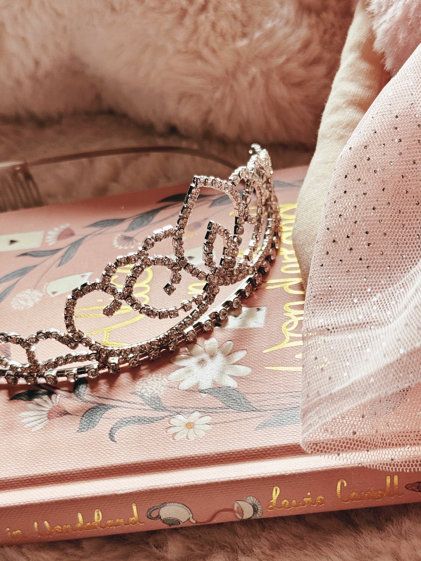 Silver rhinestone tiara set against a pink decorative book and pink fabric
