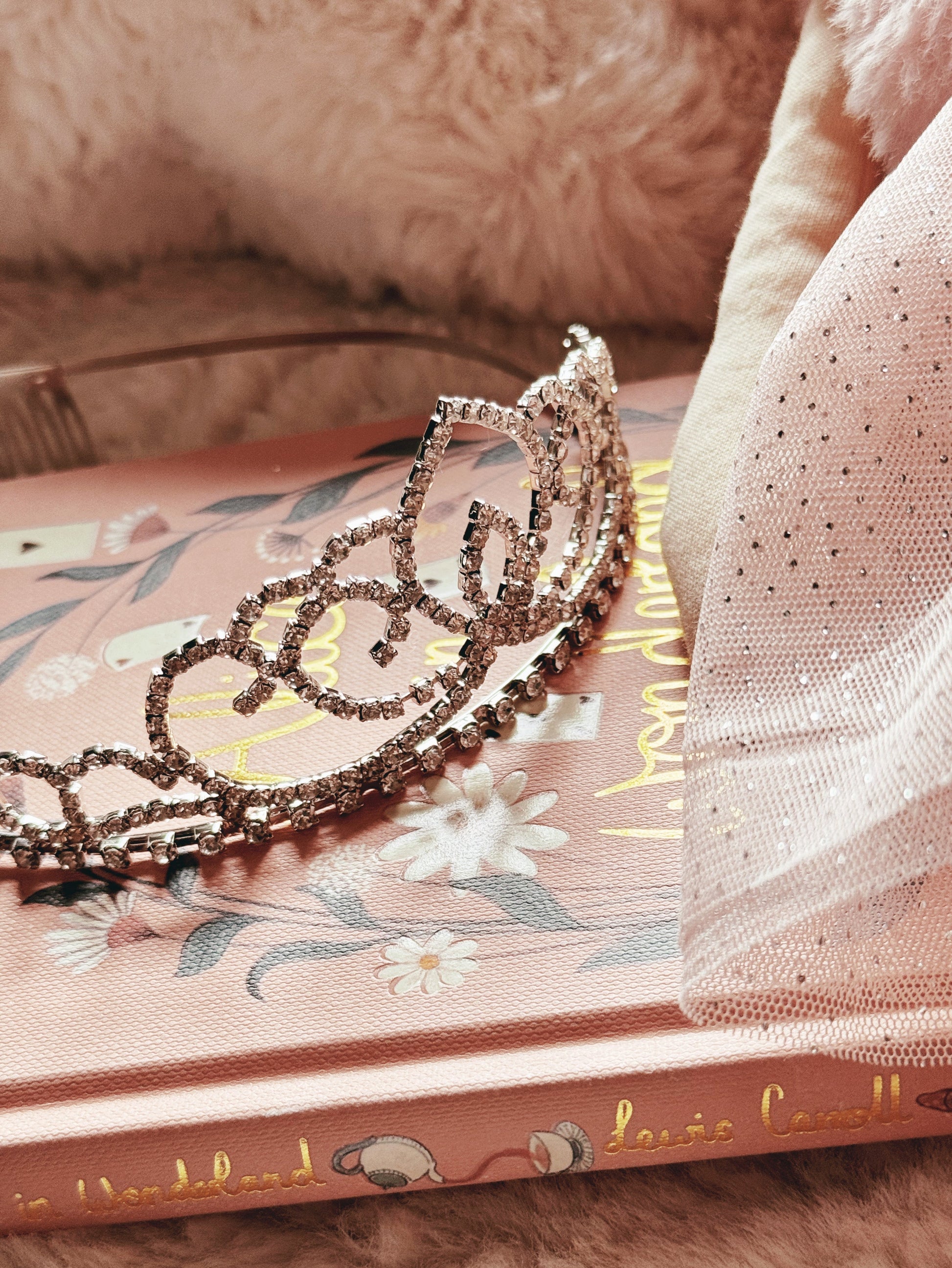 Silver rhinestone tiara set against a pink decorative book and pink fabric