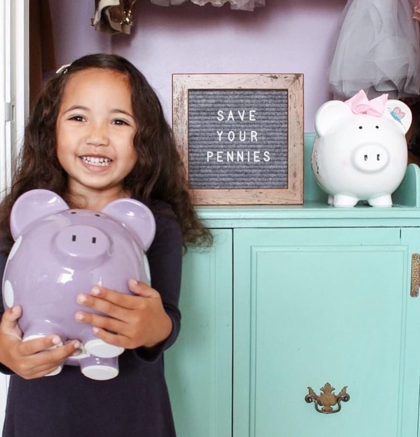 Smiling young girl holding a large purple polka dot piggy bank in a cozy room setting