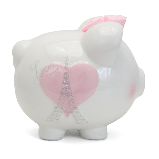 Side view of white ceramic piggy bank with pink heart and glittery Eiffel Tower design, adorned with a pink bow on its ear