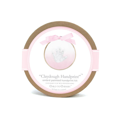 Round cardboard package of Ombre Claydough Handprint Kit with pink ribbon and white baby handprint image
