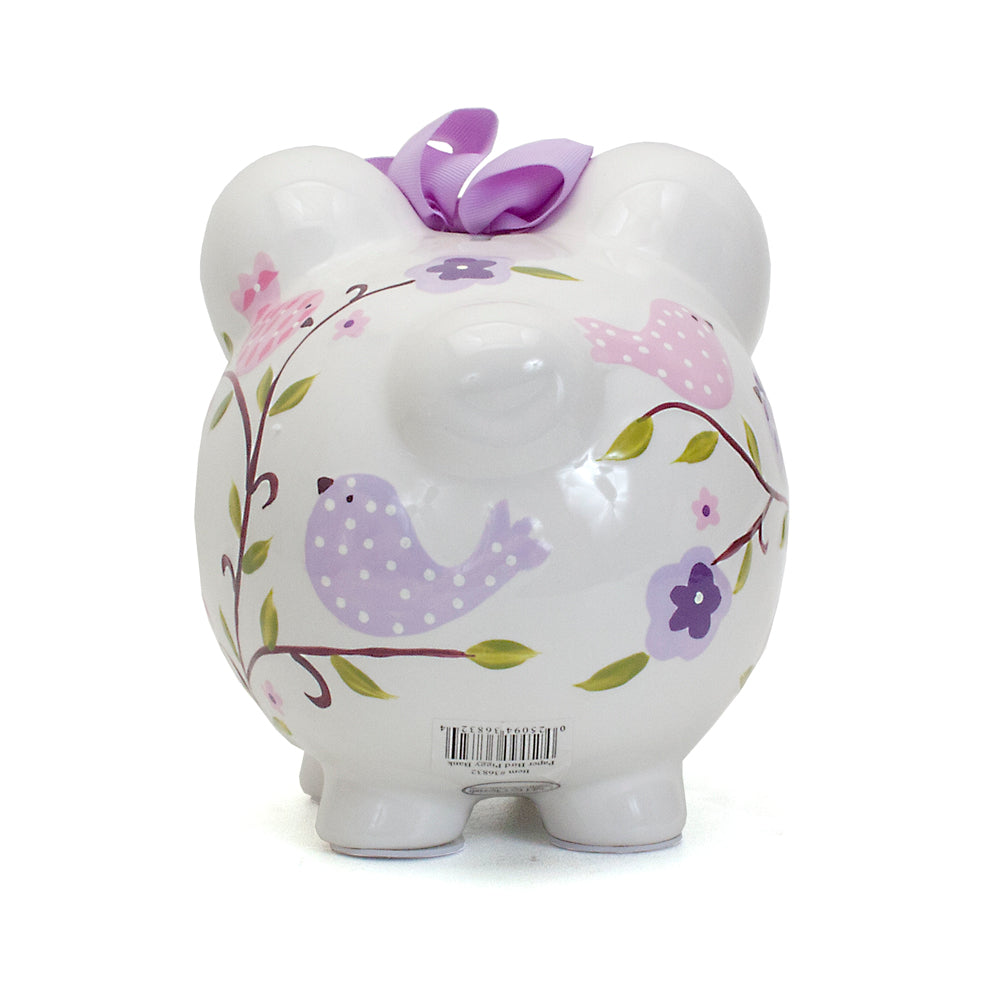 Back view of white ceramic piggy bank with pink and purple birds on branches and floral decor