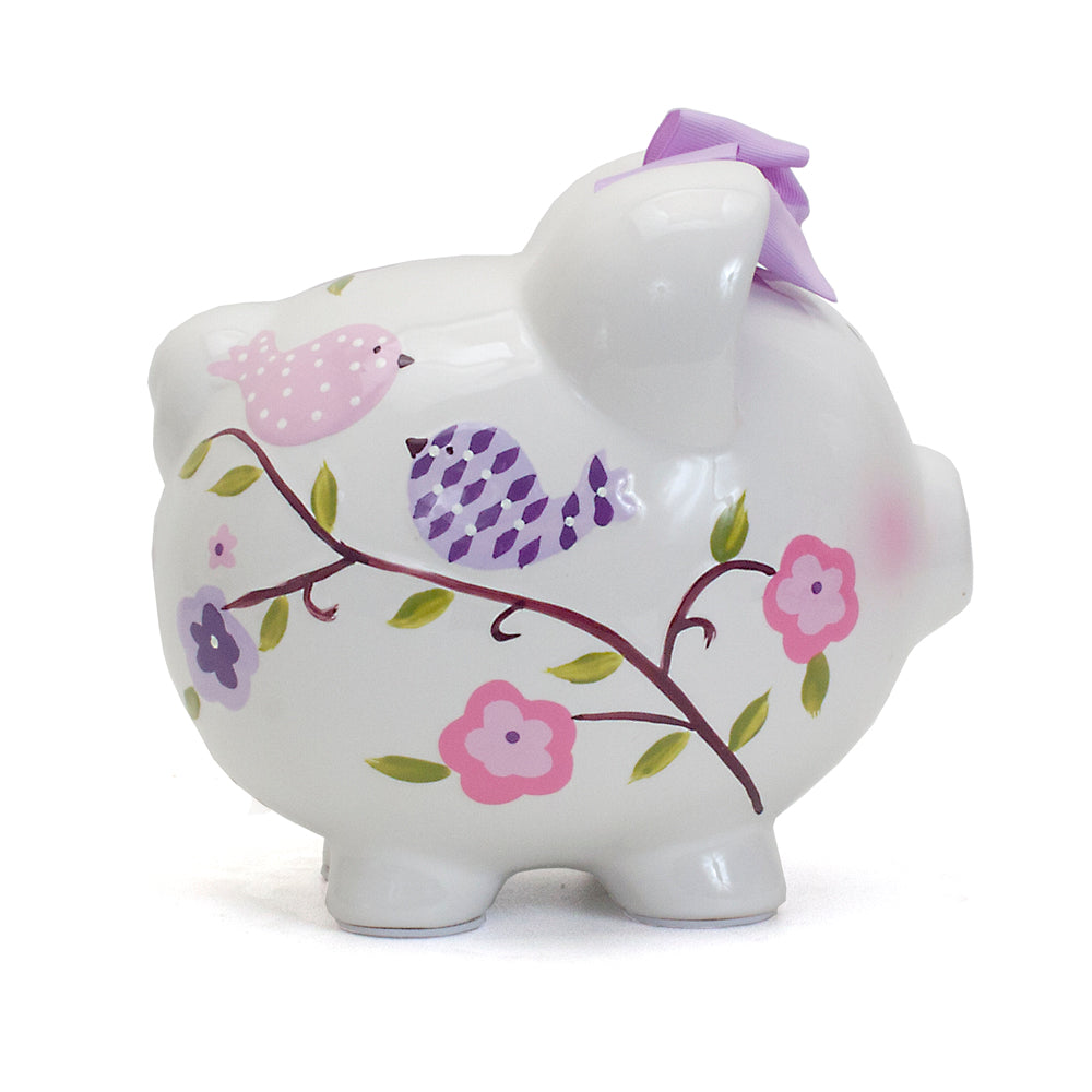 Side view of white ceramic piggy bank featuring handpainted pink and purple birds and flowers