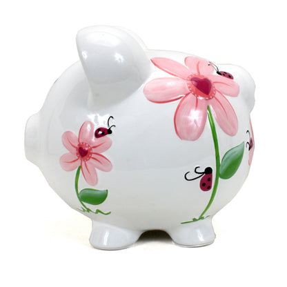 Left side angle of white ceramic piggy bank with colorful ladybug and flower artwork