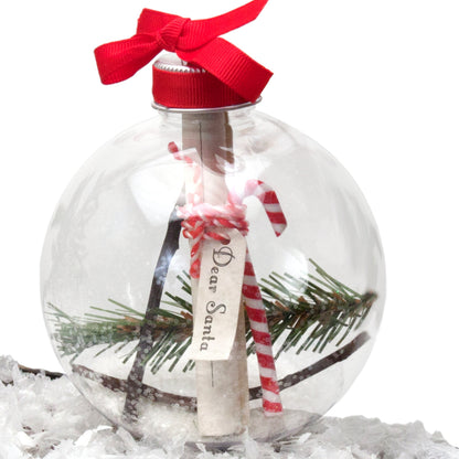 Clear shatterproof ornament filled with pine sprigs, candy cane, and scroll message inside, topped with red ribbon