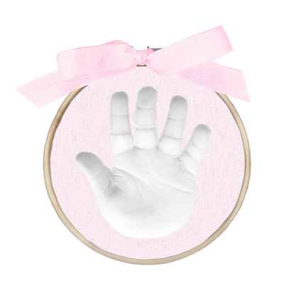 Completed handprint in white clay on pink glitter background with wooden ring and pink ribbon bow