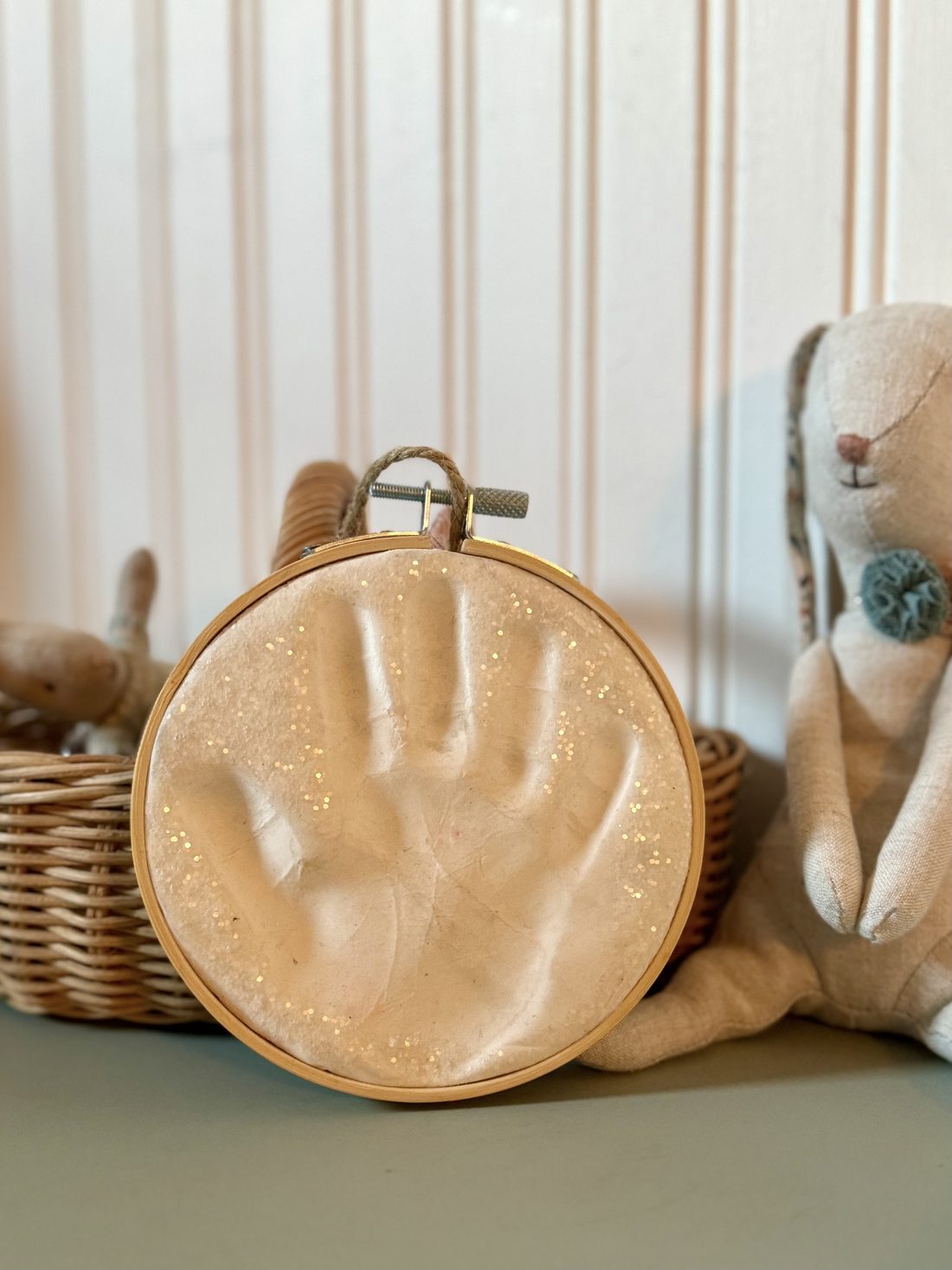 Claydough handprint keepsake on a nursery shelf with a linen bunny